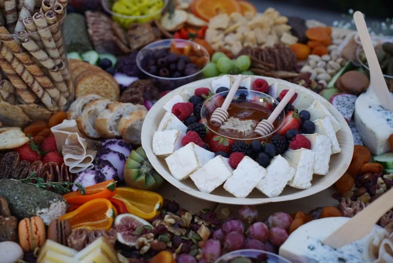 Brie, berries, honey, cured meats, sliced bread, and fruit on a charcuterie grazing table